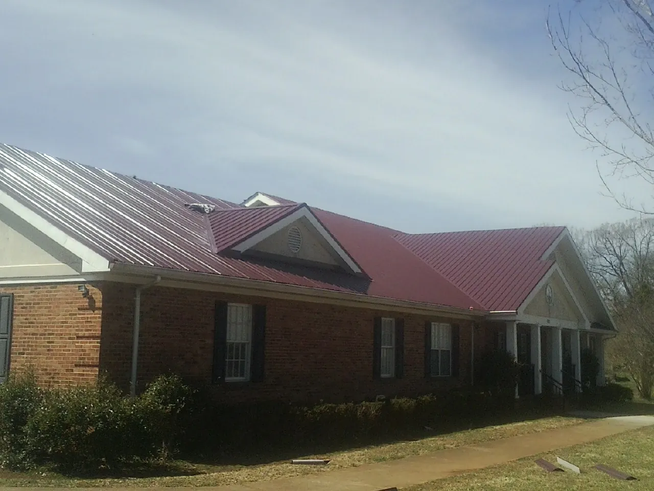Red metal roof with gabled entries on a long brick building, from a Hail Damage Roof Repair job in Glen Allen