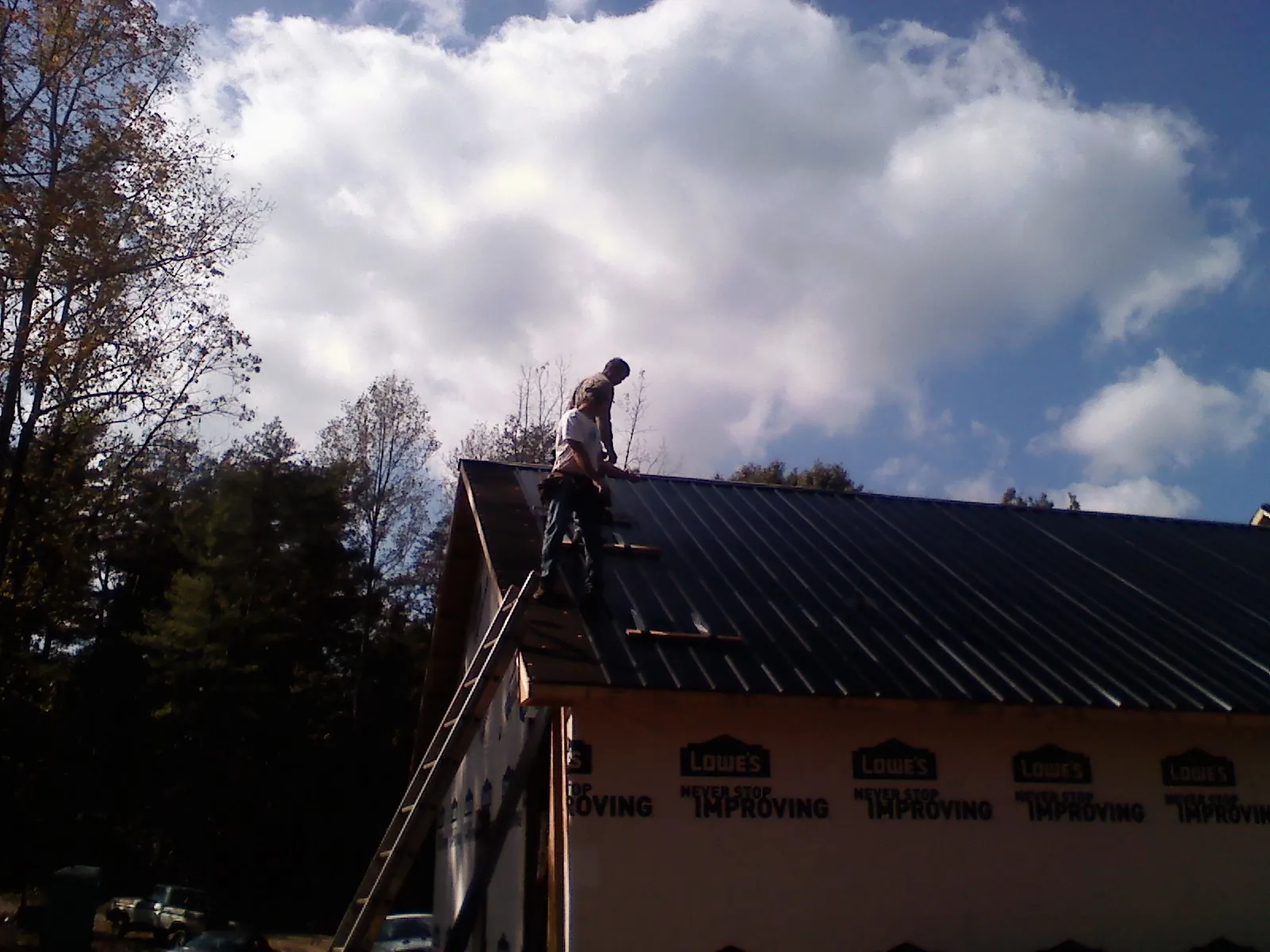 Roofer fastening dark metal panels high against a cloudy sky, from a Roof Inspection job in Glen Allen