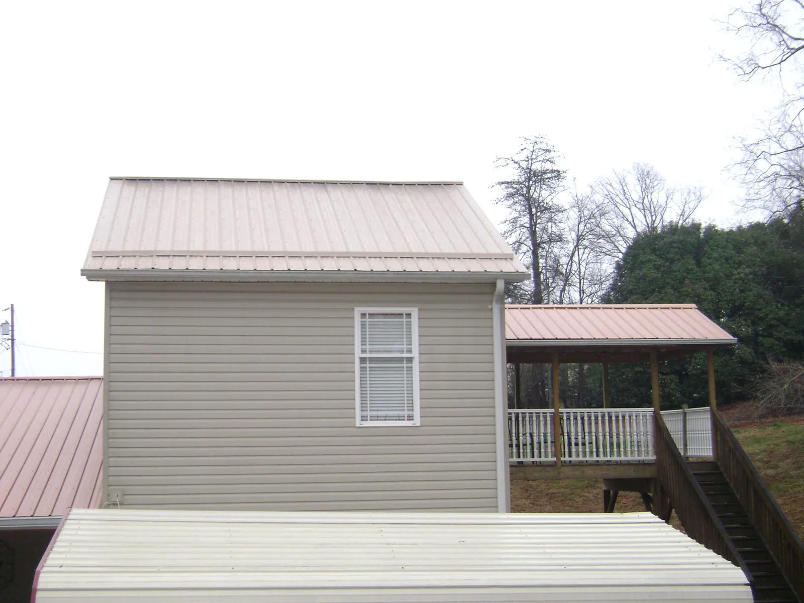 Tan metal roofs on a two story addition and attached porch, from a Roof Replacement job in Glen Allen